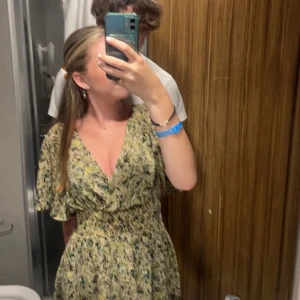 Mönstrad kortklänning från ZARA - Säljer en kortklänning från ZARA med v-ringning och smockad midja. Klänningen har ett abstrakt mönster i beige, svart, grön och gul med korta ärmar. 