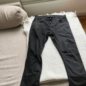 Svarta jeans från Nudie Jeans - Säljer ett par svarta jeans från Nudie Jeans i ekologisk bomull. Klassisk femficksmodell med knäppning fram och raka ben. Snygga och stilrena jeans som passar till det mesta. Storlek w30.