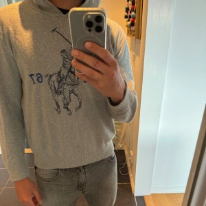 Grå hoodie från Polo Ralph Lauren med broderad polospelare - Säljer en grå hoodie från Polo Ralph Lauren med stor broderad polospelare och texten RL 67 på bröstet. Tröjan har huva och ribbade muddar vid ärmslut och nederkant. Väldigt unik Hoodie ser inte många exemplar av just denna modell tröjan är använd fåtal gånger!! Tröjan är Xl barn som motsvarar S Hör av er för eventuella frågor! 