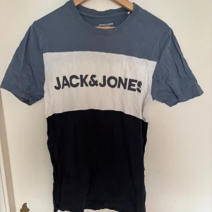 Flerfärgad t-shirt från Jack & Jones - Säljer en snygg t-shirt från Jack & Jones med färgblock i blått, vitt och svart. Stor logga framtill. Klassisk passform och rund hals. Perfekt till jeans eller shorts.