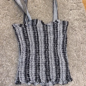 Svartvit mönstrad linnetopp från H&M Divided - Säljer en svartvit smockad linnetopp från H&M Divided med knytbara axelband och vågiga kanter nertill. Toppen har ett grafiskt mönster i svart och vitt och är stretchig och bekväm. Perfekt till sommaren!