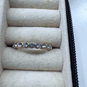 Guldfärgad ring med klara stenar - Säljer en snygg guldfärgad ring med infattade klara stenar runt hela ringen. Ringen har en unik, räfflad design på sidorna som ger den extra karaktär. Perfekt för dig som gillar smycken som sticker ut lite extra.