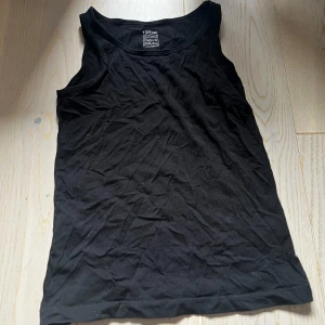 Ett Svart linnetopp från KappAhl för barn  - Säljer en enkel svart linnetopp från KappAhl, kollektionen Our Best Basics. Toppen är tillverkad i ekologisk bomull och har en klassisk ärmlös design med rund halsringning. Perfekt basplagg till garderoben. Detta plag är för barn mellan 8-10år