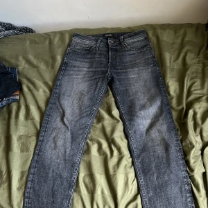 Svarta tapered jeans från Jack & Jones - Säljer ett par svarta jeans från Jack & Jones med tapered fit. Jeansen har klassisk femficksdesign, knappgylf och snygga slitningar för en cool look. Perfekta för dig som gillar en smalare passform men ändå vill ha lite utrymme vid benen.
