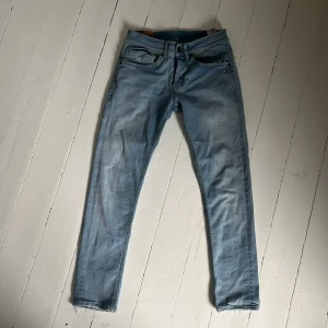 Ljusblå jeansbyxor - Säljer ett par ljusblå jeans med klassisk femficksdesign och normal passform. Jeansen har dragkedja och knapp i gylfen samt diskreta slitningar vid fickorna. Perfekta för en avslappnad stil.