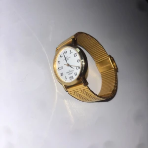 Vintage Tidéna 1881 Damur - Stilren guldfärgad klocka från Tona med vit urtavla och tydliga svarta siffror. Klockan har ett klassiskt runt ur och ett elegant metallarmband i guld. Perfekt accessoar för att lyfta din outfit.