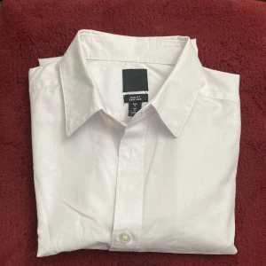 Vit skjorta med slim fit - Snygg vit skjorta i slim fit med klassisk krage och knappar framtill. Perfekt för en stilren look. Lätt att stryka och passar till många tillfällen.