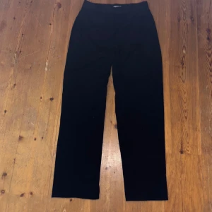 Svarta kostymbyxor från Ellos - Snygga svarta kostymbyxor från Ellos med hög midja och raka ben. Byxorna har en stilren design med knäppning fram och är perfekta för en chic look.