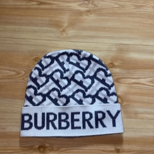 Mönstrad mössa från Burberry - Snygg mössa från Burberry med ett stilrent mönster i svart och vitt. Mössan har en bred uppvikt kant med Burberry-loggan tydligt broderad. Perfekt för att hålla stilen i kallare väder.