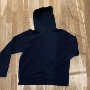 Marin blå hoodie från Ralph Lauren - Säljer en stilren marin blå hoodie från Ralph Lauren med en diskret logga på bröstet. Perfekt för en avslappnad look. Hoodien en klassisk känguruficka framtill. Passar bra till både jeans och joggers. Passar folk i längd 160-170