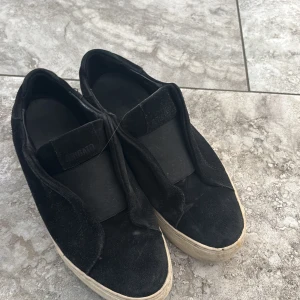Svarta sneakers från Arigato - Säljer ett par svarta sneakers från Arigato. Skorna har en stilren design med en överdel i mocka och en vit sula. Perfekta för en avslappnad stil.