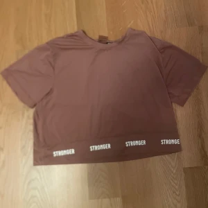 Stronger topp i rosa 🩷 - Säljer denna gammalrosa träningstopp från Stronger, lite Croppad och oversized passform med vit text i midjan. Sällan använd 🩷passar bra för rörlig aktivitet!