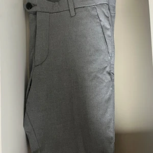 Grå kostymbyxor - Snygga grå kostymbyxor med en klassisk design. Byxorna har en midwaist passform och är utrustade med knappar och bälte för en stilren look. Perfekta för en formell stil.