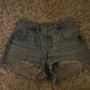Blå jeansshorts från Levi's - Snygga blå jeansshorts från Levi's med slitna detaljer. De har en klassisk femficksdesign och knappgylf. Perfekta för en avslappnad stil.