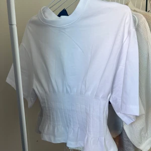 Vit t-shirt från Gina Tricot - Säljer en stilren vit t-shirt från Gina Tricot i storlek XS. T-shirten har en unik plisserad design som ger en snygg twist till en klassisk look. Perfekt för att lyfta din vardagsstil!