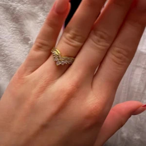 Guldfärgad ring med glittriga detaljer - Elegant guldfärgad ring med en unik design som har glittriga detaljer. Perfekt för att ge en touch av glamour till din stil. Ringen har en v-formad design som ger den en modern och stilren look.