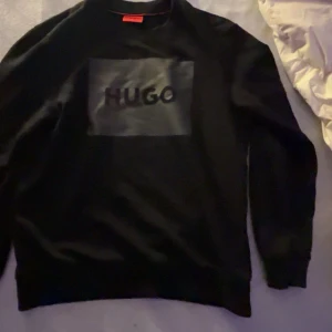 Svart tröja från Hugo - Säljer en stilren svart tröja från Hugo med ett stort tryck på framsidan. Tröjan har långa ärmar och en klassisk passform. Perfekt för en avslappnad look. 