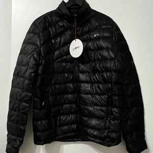 Svart dunjacka från Yeti - Säljer en svart dunjacka från Yeti med dragkedja och Crystal Down-fyllning. Jackan är lätt och perfekt för kyliga dagar. Den har en stilren design med Yeti-logga på bröstet och är långärmad. Passar perfekt för höst och vinter.