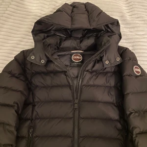 Colmar jacka - Säljer en svart pufferjacka från Colmar med huva och dragkedja. Jackan har långa ärmar och är perfekt för kyligare väder. Den är quiltad för extra värme och stil.