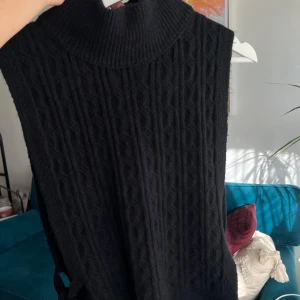 Svart stickad väst med knyt - Snygg svart stickad väst med hög krage och knytband på sidorna. Perfekt för lager-på-lager-stil och ger en trendig touch till din outfit. XS-S