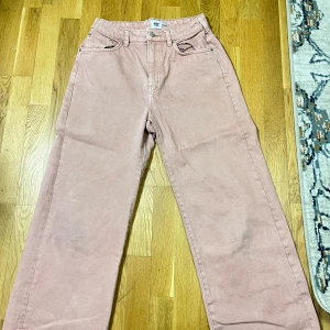 Rosa byxor med raka ben - Säljer ett par rosa byxor med raka ben och hög midja. Byxorna har en klassisk design med fickor fram och bak samt en knapp och dragkedja i gylfen. Perfekta för en avslappnad stil.