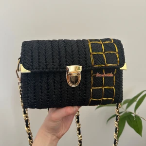 Svart handväska med gulddetaljer - Handmade av min mamma! 💝Snygg svart handväska med flätat mönster och gulddetaljer. Väskan har en elegant guldkedja som axelrem och ett stilrent spänne framtill. Perfekt för att ge en touch av glamour till din outfit. 