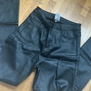 Svarta byxor i skinnimitation - Snygga svarta byxor i skinnimitation med hög midja och dragkedja. Perfekta för en trendig look. De har en klassisk femficksdesign och en smickrande passform.