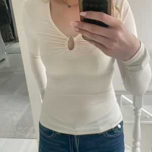 Vit långärmad topp från Hm - Säljer en stilren vit långärmad topp från hm med en v-ringning och en dekorativ rynkning framtill. Perfekt för en chic och enkel look. Passar bra till både jeans och kjol.