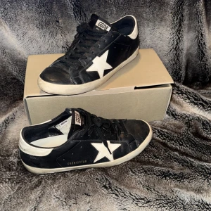 Golden Goose skor - Snygga svarta sneakers från Golden Goose med vit stjärndetalj på sidan och vit häl. Skorna har en klassisk design med snörning och en bekväm passform. Perfekta för en stilren look. Box och dust bag finns✅