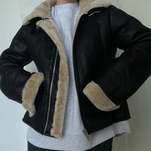 Svart skinnjacka med foder från NA-KD - Snygg svart skinnjacka från NA-KD med mjukt beige foder. Jackan har dragkedja framtill och på fickorna samt en klassisk krage. Perfekt för kyligare dagar.