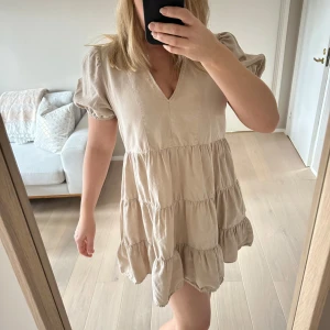 Zara strl XS beige volangklänning linneklänning - Säljer en söt beige klänning från Zara med volanger och v-ringning. Klänningen har korta puffärmar och en luftig passform, perfekt för varma dagar. Klänningen jag har på bilden är S. Säljer denna som är XS som var för liten för mig.