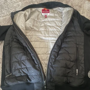 Svart jacka från Parajumpers - Säljer en svart jacka från Parajumpers med quiltad design och dragkedja. Jackan har långa ärmar och ribbade muddar. Perfekt för kyligare dagar med sin fleecefoder. Märkeslogga på ärmen ger en cool touch.