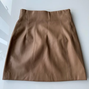 Beige kjol - Snygg beige kjol i skinnimitation med stilrena sömmar framtill. Kjolen har en enkel och clean design som passar perfekt till en cool vardagslook. Rak passform och midjehög modell