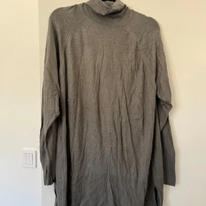 Grå polotröja i längre modell - Mysig grå polotröja med lång ärm och ribbade muddar. Tröjan är oversized och har en hög polokrage. Modellen är i längre modell.