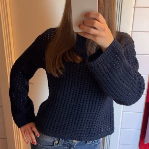 Mörkblå stickad tröja Holly White - Säljer en mörkblå stickad tröja från Holly White i storlek XS. Tröjan har ett grovmaskigt, håligt mönster och är långärmad med ribbade muddar. Perfekt för lager-på-lager. (Har linne under tröjan på bilden). Säljer då tröjan blivit för liten
