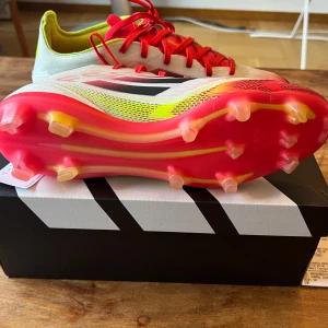 Adidas F50 PRO Pure victory  - Adidas fotbollsskor med vit ovandel, neon-gula detaljer och röda snören. Sulan är röd med gula inslag och har fasta dobbar för gräsplan. Skorna har använt ca 5 gånger och säljs för att skorna inte passa. Kvitto kartong finns med.                                                                       Pris kan diskuteras 