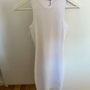 Vit ribbad kortklänning - Säljer en vit, ribbad och tight kortklänning från FB Sister. Klänningen är ärmlös med rund halsringning och har en enkel, stilren design som sitter snyggt på kroppen. Perfekt för dig som gillar minimalistisk och fräsch stil. Aldrig använd 