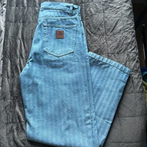 Randiga blå jeans från Carhartt - Säljer ett par ljusblå jeans från Carhartt med diskreta vertikala ränder. Klassisk femficksmodell med Carhartt-läderpatch på bakfickan. Byxorna har raka ben och är tillverkade i slitstarkt bomullsjeans. Perfekta för en chill och stilren look.