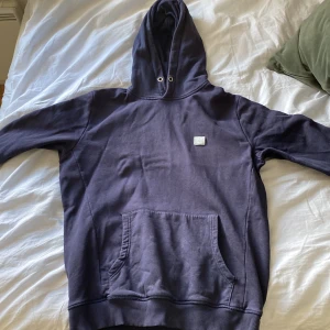 Mörkblå hoodie från Les Deux, storlek L - Snygg mörkblå hoodie från Les Deux i storlek L. Klassisk modell med huva, känguruficka och broderad patch på bröstet. Mjuk insida och ribbade muddar. Perfekt för chill dagar eller när du vill ha en clean streetstyle.