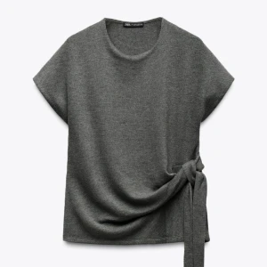 topp med knyt från Zara - Snygg grå topp från Zara med korta ärmar och rund hals. Toppen har en cool knytdetalj i sidan som ger en extra touch till looken. Perfekt att styla med jeans eller kjol för en chill vibe. Har fof prislapp på