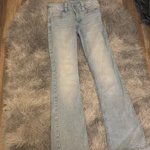 Ljusblå bootcut jeans med fickdetaljer - Snygga ljusblå jeans med bootcut passform och coola fickor med lock och knapp bak. Jeansen har klassisk femficksdesign, breda hällor och är tillverkade i mjukt denim. Perfekta för dig som gillar en avslappnad men trendig look.