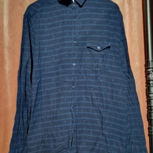 Blå randig skjorta Made in the Shade - Snygg blå skjorta från Made in the Shade i storlek L. Skjortan har horisontella ränder och små ankare som mönster, klassisk krage, bröstficka med knapp och långa ärmar. Perfekt för dig som gillar en chill och stilren look.