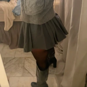 Grå plisserad kortkjol - Supersnygg grå plisserad kortkjol med klassisk skoluniform-vibe. Kjolen har en hög midja och ger en riktigt trendig look, perfekt att styla med boots eller stickad tröja. Enkel att matcha och ger en cool siluett.