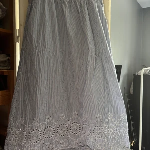 Randig blåvit kjol med spets - Supersöt kjol i blåvitt randigt tyg med broderade spetsdetaljer längst ner. Kjolen har en luftig passform och är perfekt för varma dagar. Materialet känns som bomull och mönstret är klassiskt och fräscht.