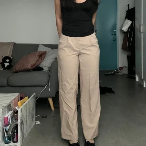 Beiga vida kostymbyxor i bomull - Snygga beiga kostymbyxor med hög midja och raka, vida ben. Byxorna är tillverkade i bomull och har en klassisk look som passar perfekt till en stilren outfit. De har diskreta fickor och stängs med dragkedja och knapp framtill.