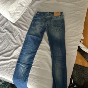 Blå jeans från Jack & Jones, 28/32 - Snygga blå jeans från Jack & Jones med klassisk tvätt och lätt slitning. Modellen har raka ben, fem fickor och detaljerade sömmar. Perfekt passform för dig som gillar en stilren och tidlös look. Storlek 28/32.