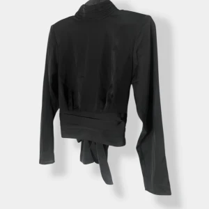 Svart silkeslen topp från Gina Tricot – strl 36, öppen rygg, aldrig använd - Säljer en svart topp från Gina Tricot i storlek 36, men den passar även dig som har storlek 38. Den är helt ny och aldrig använd. Toppen är gjord i silkeslen polyester som känns mjuk och lyxig mot huden.  Modellen är elegant och tidlös med öppen rygg och ett fint band som kan knytas på flera olika sätt, perfekt som festtopp eller till vardags med ett par jeans eller kjol. Den svarta färgen gör den enkel att matcha och passar i både en klassisk och trendig garderob. Ett riktigt fint plagg för dig