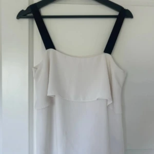 Vitt linne med svarta axelband - Stilrent vitt linne med svarta axelband och volangdetalj framtill, från H&M. Perfekt för varma dagar nu k sommar! Materialet känns lätt och luftigt, och volangen ger en extra touch till looken.