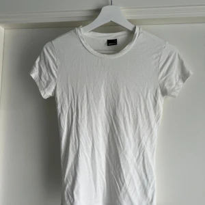 Vit soft touch t-shirt från Gina Tricot - En klassisk vit t-shirt från Gina Tricot soft touch second skin i figurnära modell. T-shirten har rund halsringning och korta ärmar. Tillverkad i mjukt och stretchigt material som känns skönt mot huden. Perfekt att styla med jeans eller kjol för en clean look.