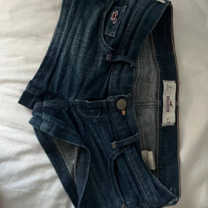Lågmidjade jeansshorts från hollister - Snygga mörkblå jeansshorts från Hollister med klassiska fickor bak och fram, samt coola detaljer och logga på fickan. Shortsen har låg midja och är perfekta för sommaren. De är gjorda i mjukt denim och har en bekväm passform.